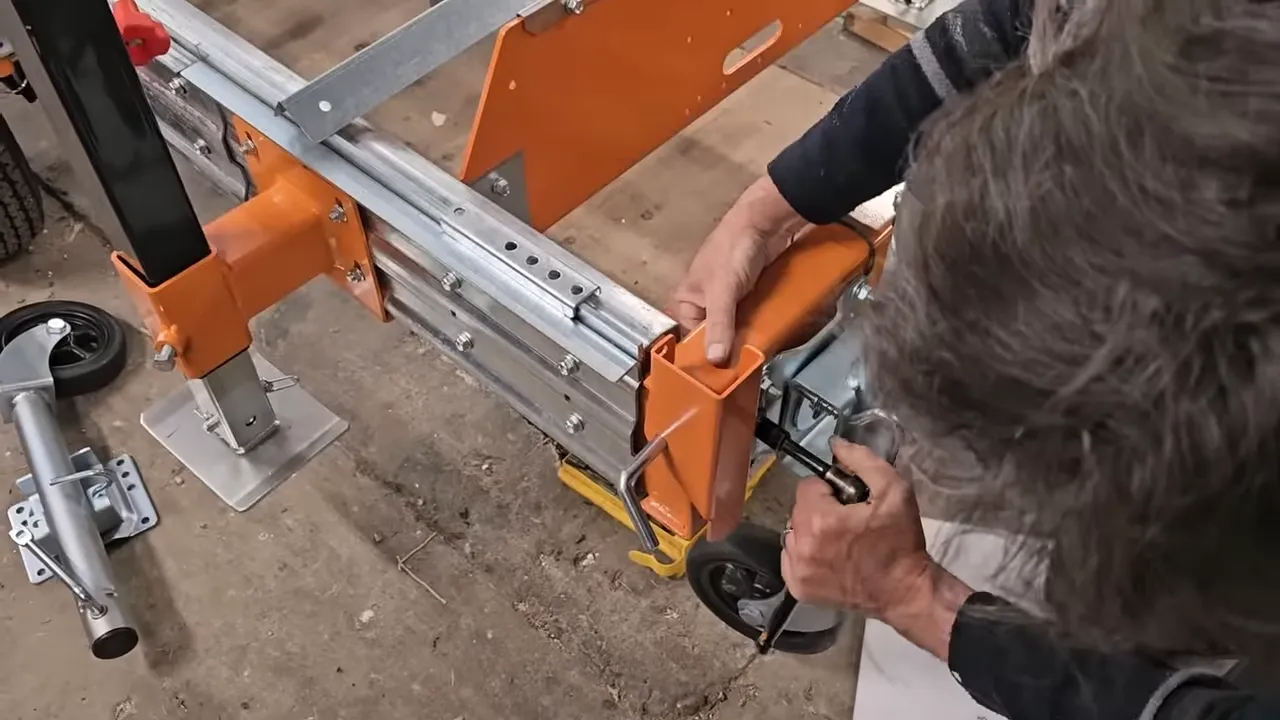 Close-up of hands adjusting a trailer jack pin and wheel on an orange norwood sawmill trailer