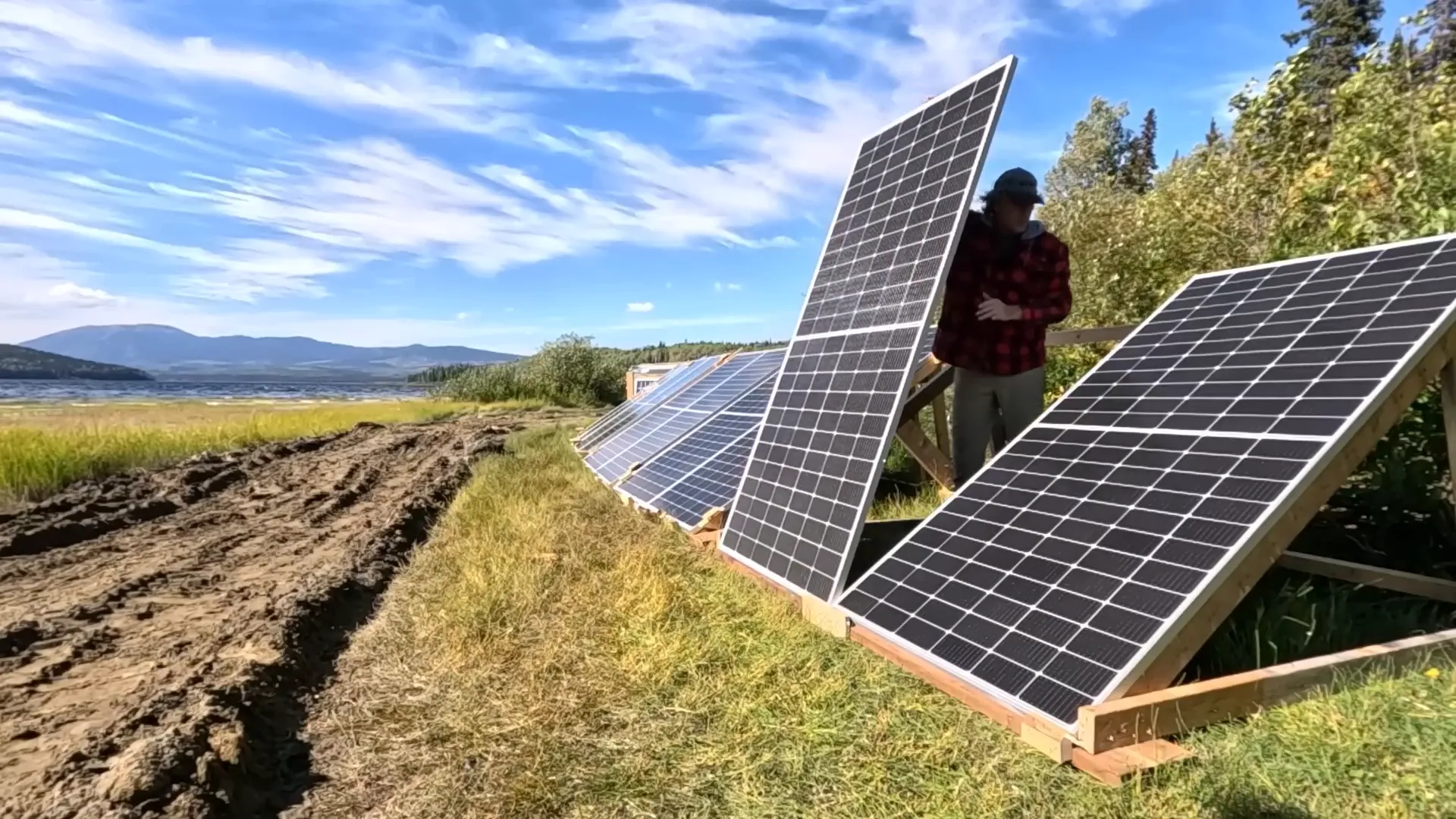 Building Our Island Homestead: A Rewarding Challenge - S2 Ep33 5 A man in installing solar panels on a wooden rack beside a lake