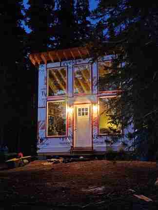 A tiny cabin at night with porch lighting, with a forested back-drop
