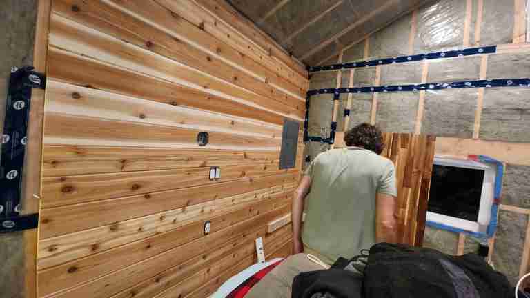 Man is installing cedar siding inside a tiny cabin
