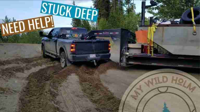 A big 4x4 truck pulling a flatdeck trailer gets stuck in the deep silt