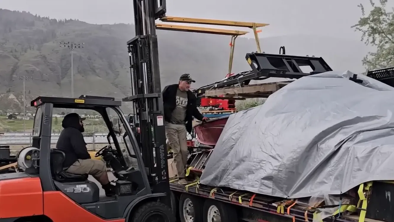 A man loads a boom lift onto a loaded trailer with the aid of a fork-lift driver