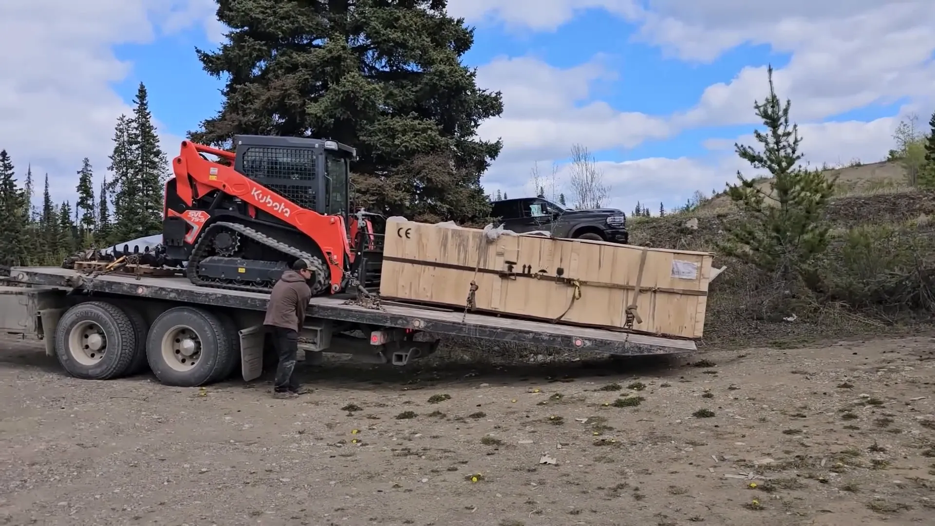 A kubota and a large crate sit atop a tilt trailer