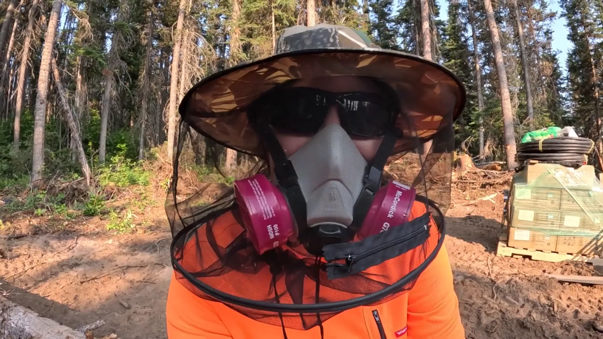 Why We Built a Shelter in the Woods - S2 Ep11 4 A woman wears a sun hat, sun glasses, mosquito netting and a full-on respirator