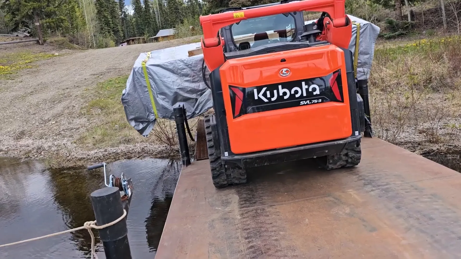 An orange kubota loads equipment onto a barge