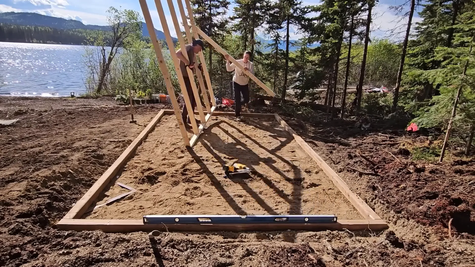 Man and woman erect the first stud wall on their new greenhouse on an off grid island