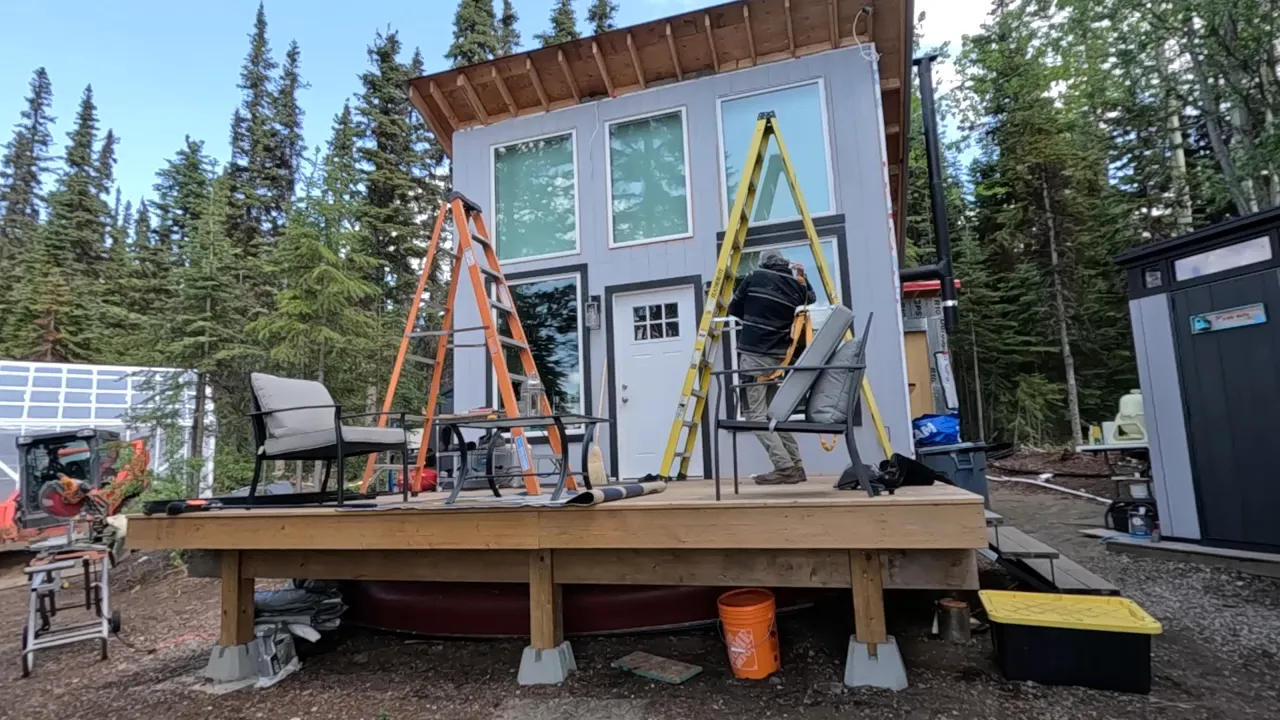 Off Grid Cabin Build: Facing Fears on Homemade Scaffolding After My Bad Fall | S4 Ep9 1 Worker wearing a safety harness on ladder installing window trim on off-grid cabin deck