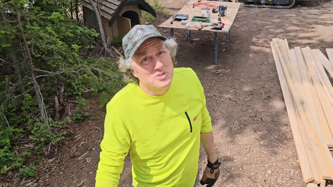 Off Grid Cabin Build: Facing Fears on Homemade Scaffolding After My Bad Fall | S4 Ep9 6 Worker looking up toward the eaves with stacked boards and a work table in the background