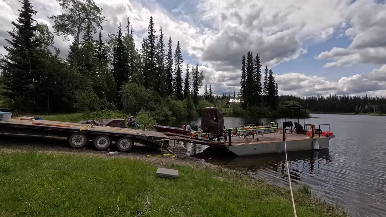 One Slip and Our New Sawmill Falls Into the Water! - S4 Ep11 10 Portable norwood sawmill secured on a barge at a lakeshore launch, trailer parked to the left and crew working on the deck