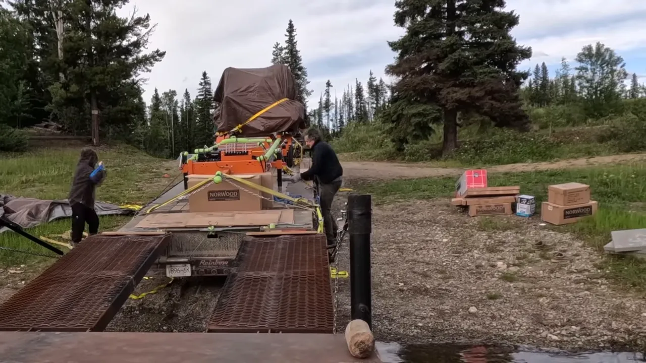 One Slip and Our New Sawmill Falls Into the Water! - S4 Ep11 9 Boxes of norwood parts and gear stacked beside a trailer with the tarped sawmill being prepared