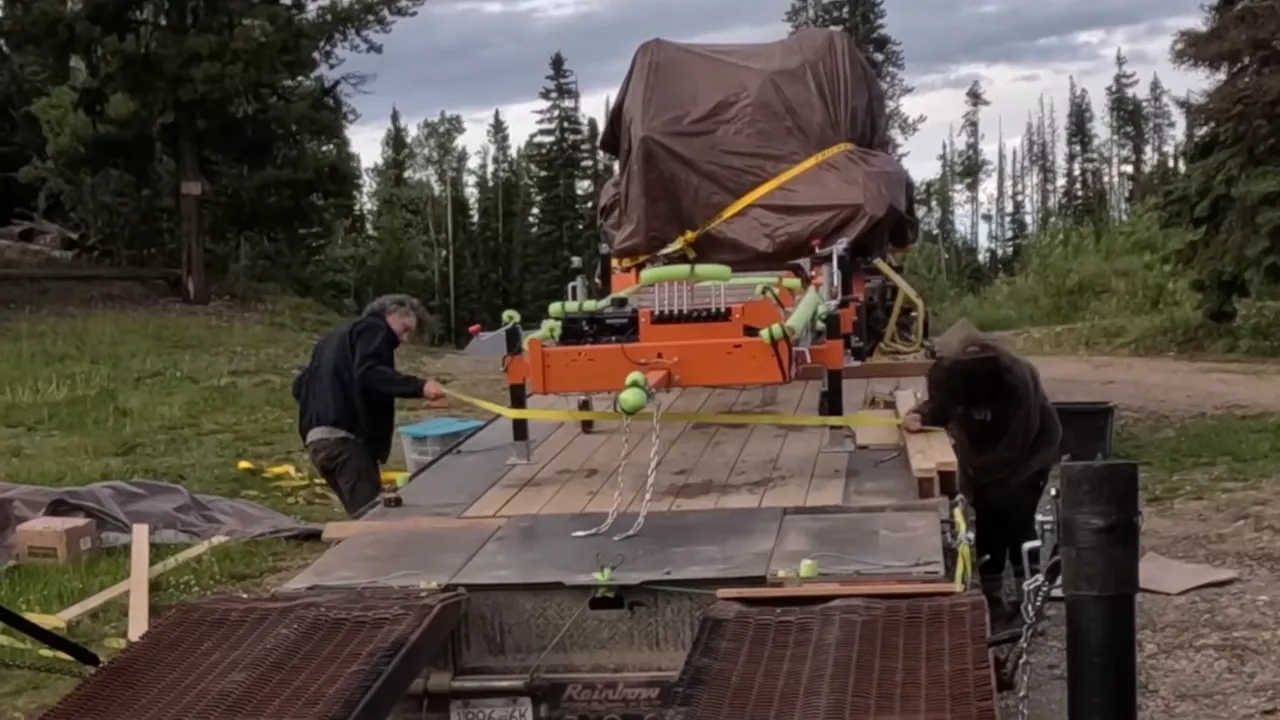 One Slip and Our New Sawmill Falls Into the Water! - S4 Ep11 5 Workers securing portable sawmill on flatbed trailer with yellow ratchet straps.