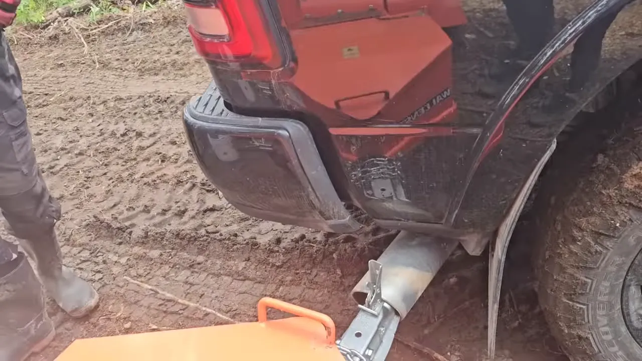 Truck rear bumper pressed against an orange wood chipper hitch with visible mud and scuffed paint