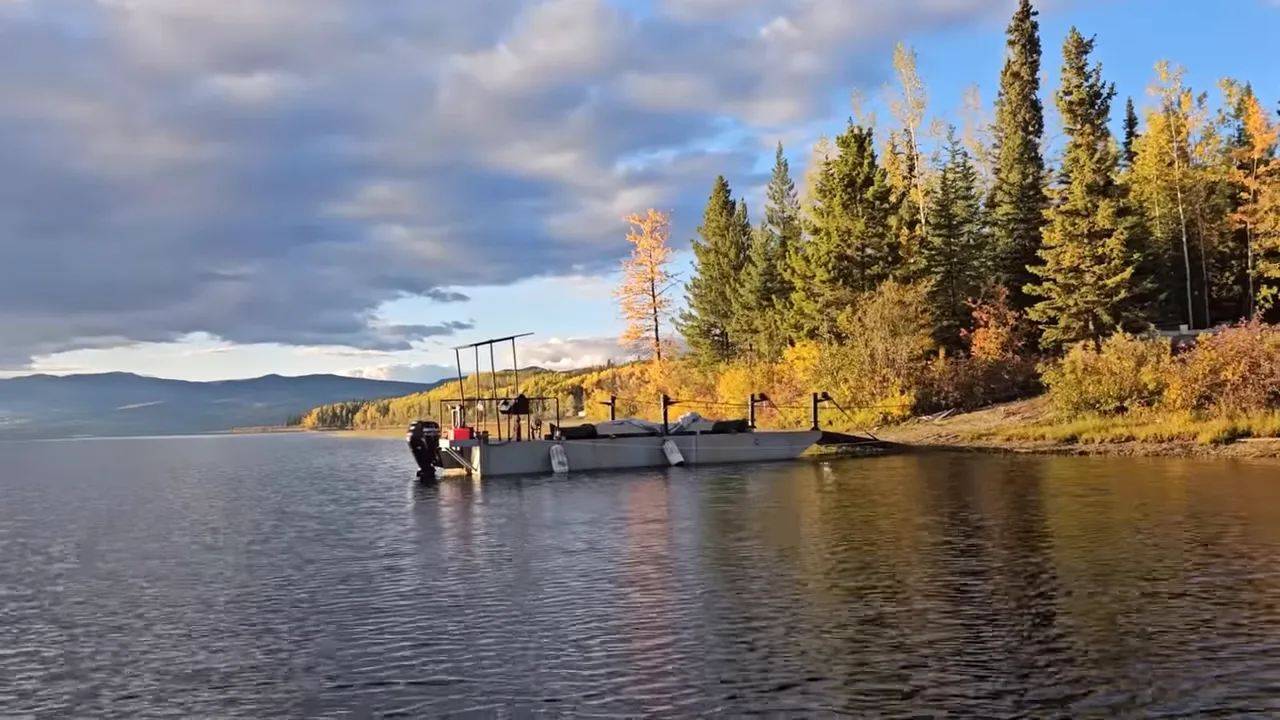 Work barge anchored close to a spruce-lined shoreline with autumn colours and calm water