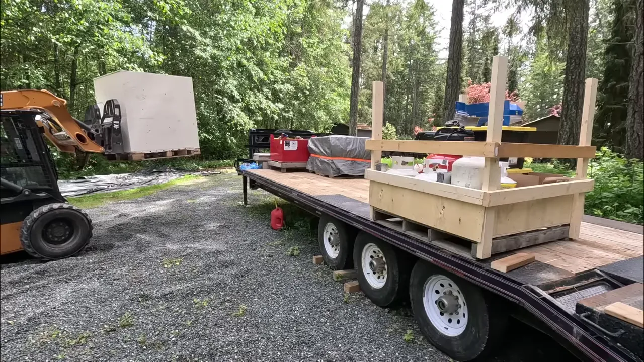 Drone shot of a pickup and fully loaded trailer driving on a remote gravel road edged by trees.