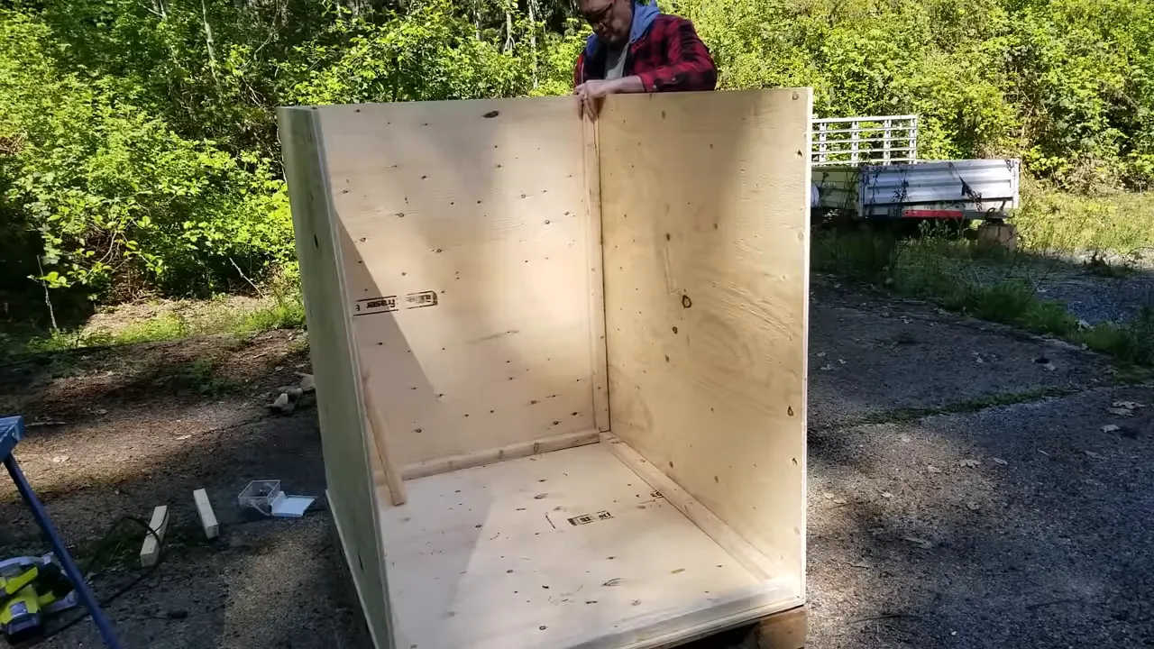 Person placing a straightedge across a plywood-covered pallet to measure and square the crate floor.