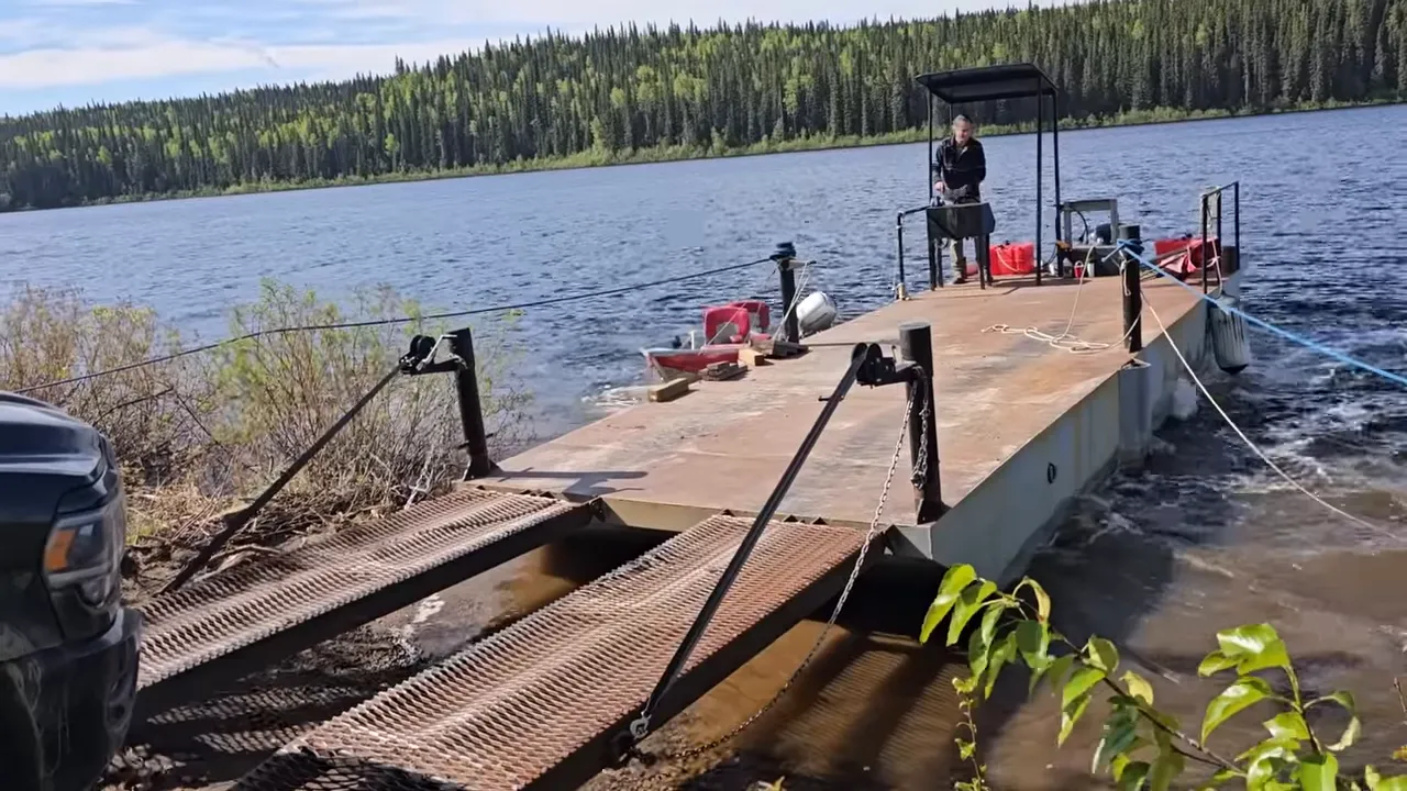 Metal loading ramps and a barge in shallow water with a person at the far end guiding the approach.