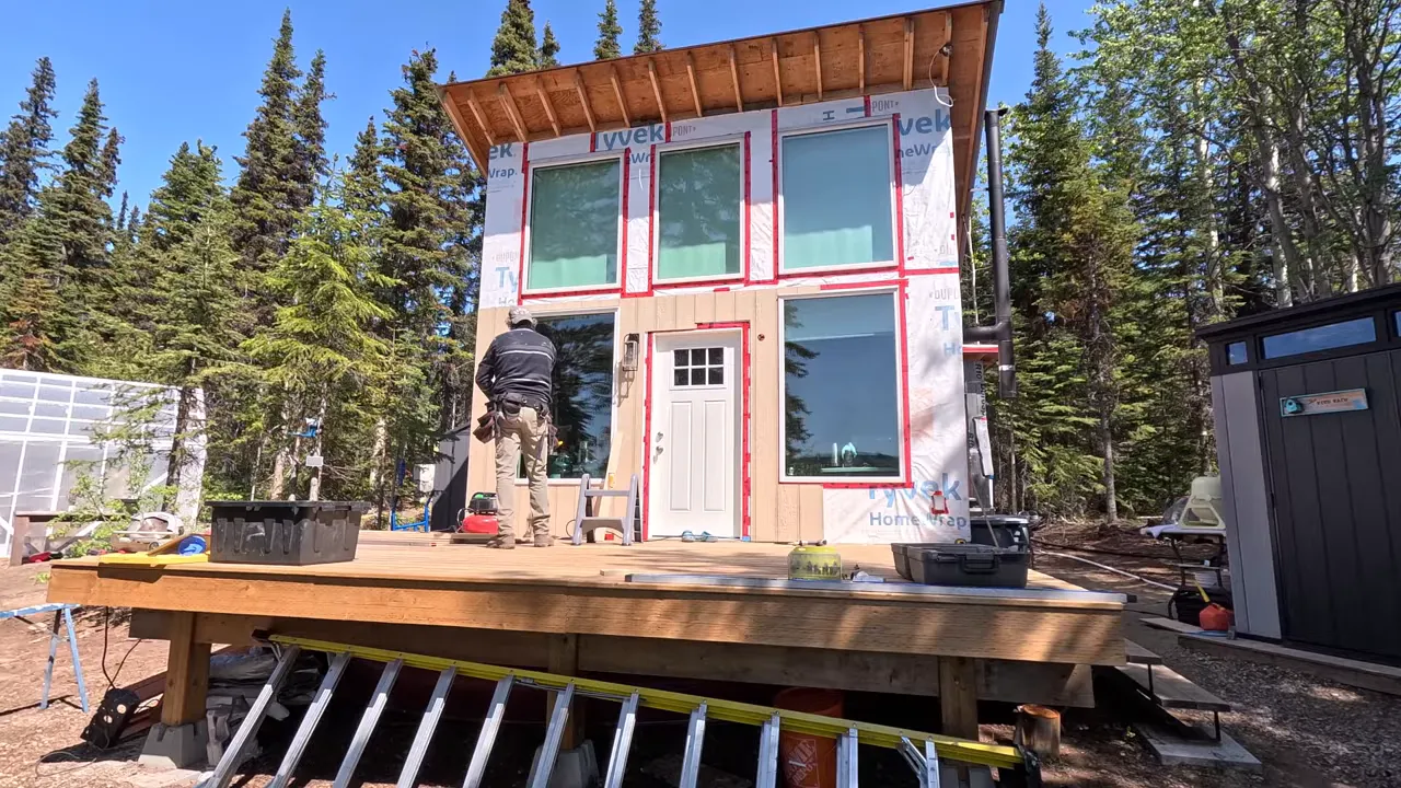 Off Grid Life Canada: Building a Tiny Cabin on Our Remote Island – Biggest Transformation Yet! - S4 Ep8 2 Worker at the front door of a tiny cabin installing trim and siding with housewrap visible