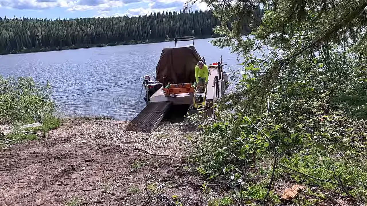 Barge beached at the shore with ramps lowered and a worker preparing the transfer