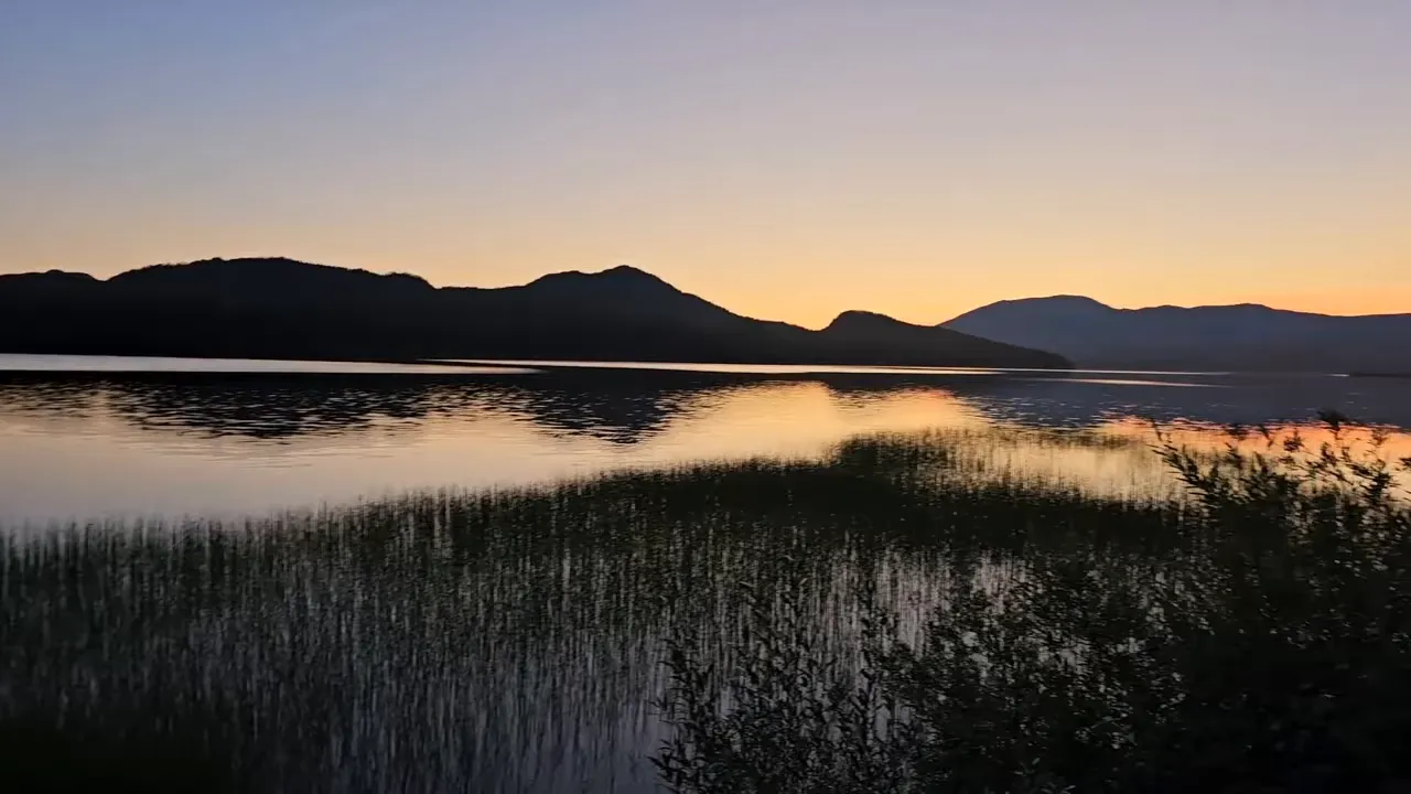 Sunset reflection on a calm remote island lake with mountain silhouettes