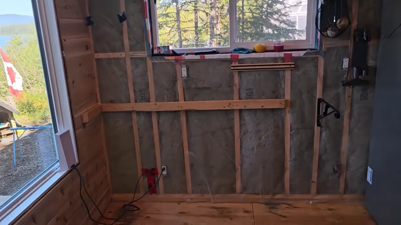 Tiny off-grid cabin interior with exposed wall framing, insulation panels, and a window above unfinished counters