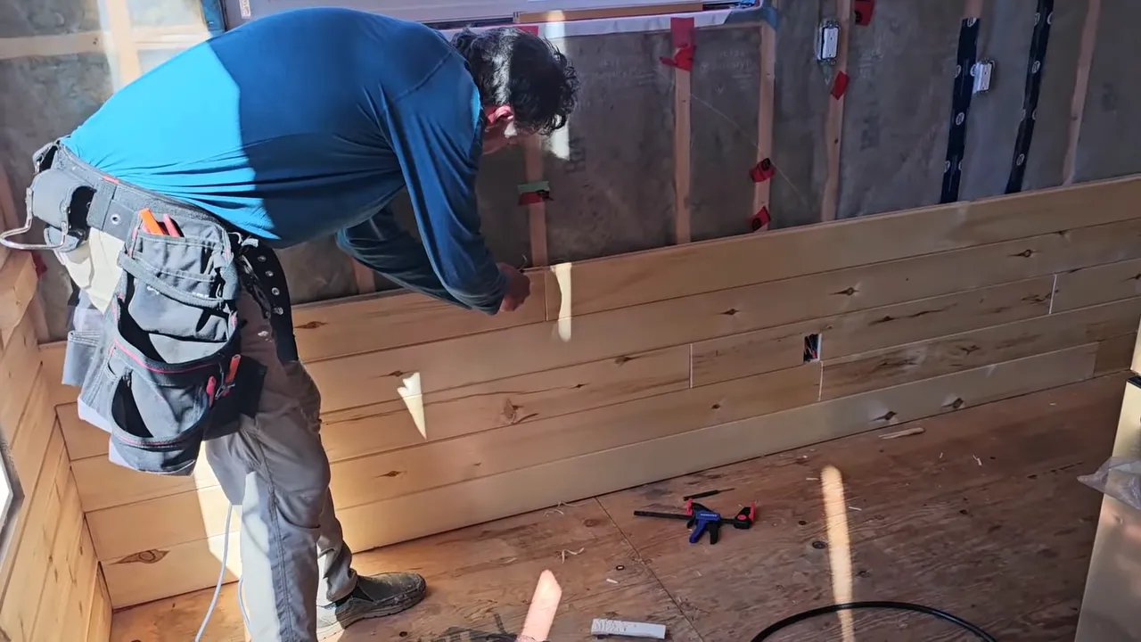 Builder measuring and installing a section of interior wall boards in a tiny off-grid cabin