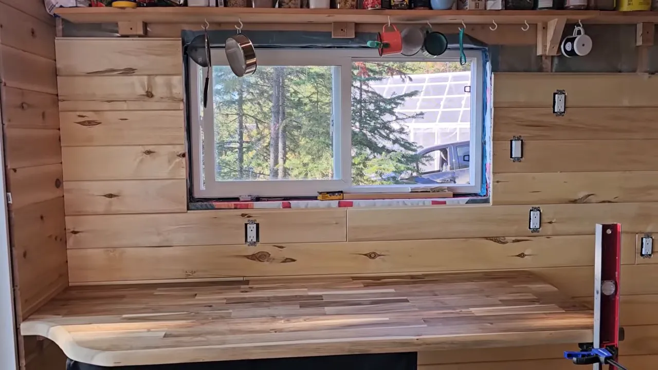 Off-grid cabin interior showing finished wall sections around an installed window and prepped floor