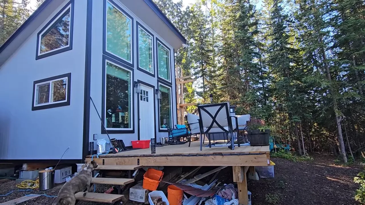 Off-grid cabin exterior with windows and deck packed with construction materials and storage tubs
