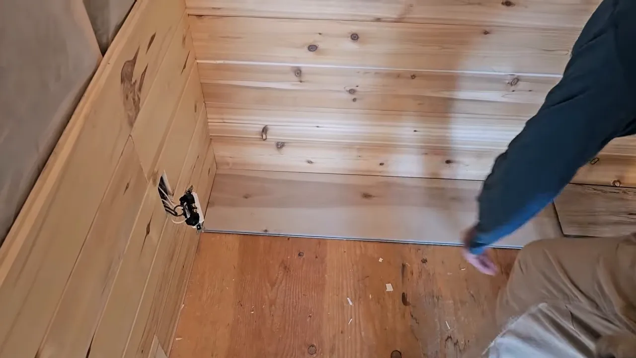 Corner view of a tiny off-grid cabin interior showing prepared walls and subfloor awaiting flooring