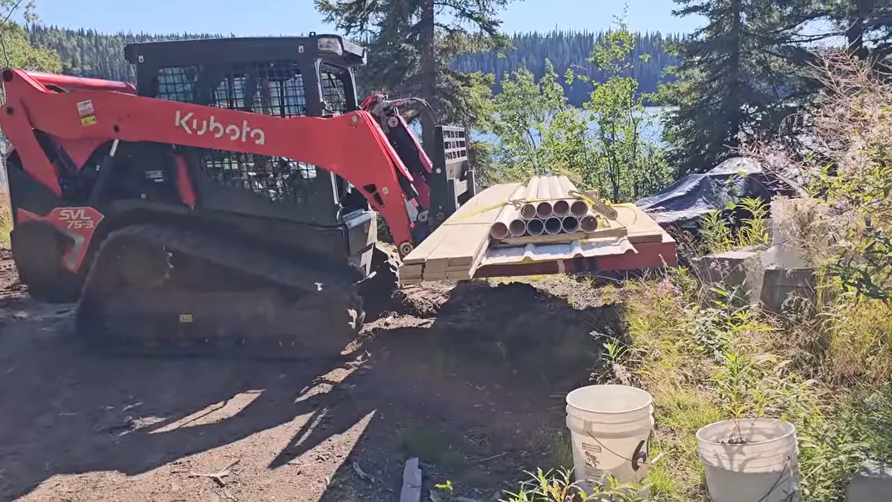 Kubota skid-steer unloading a pallet of building materials on a remote island with five-gallon buckets in the foreground