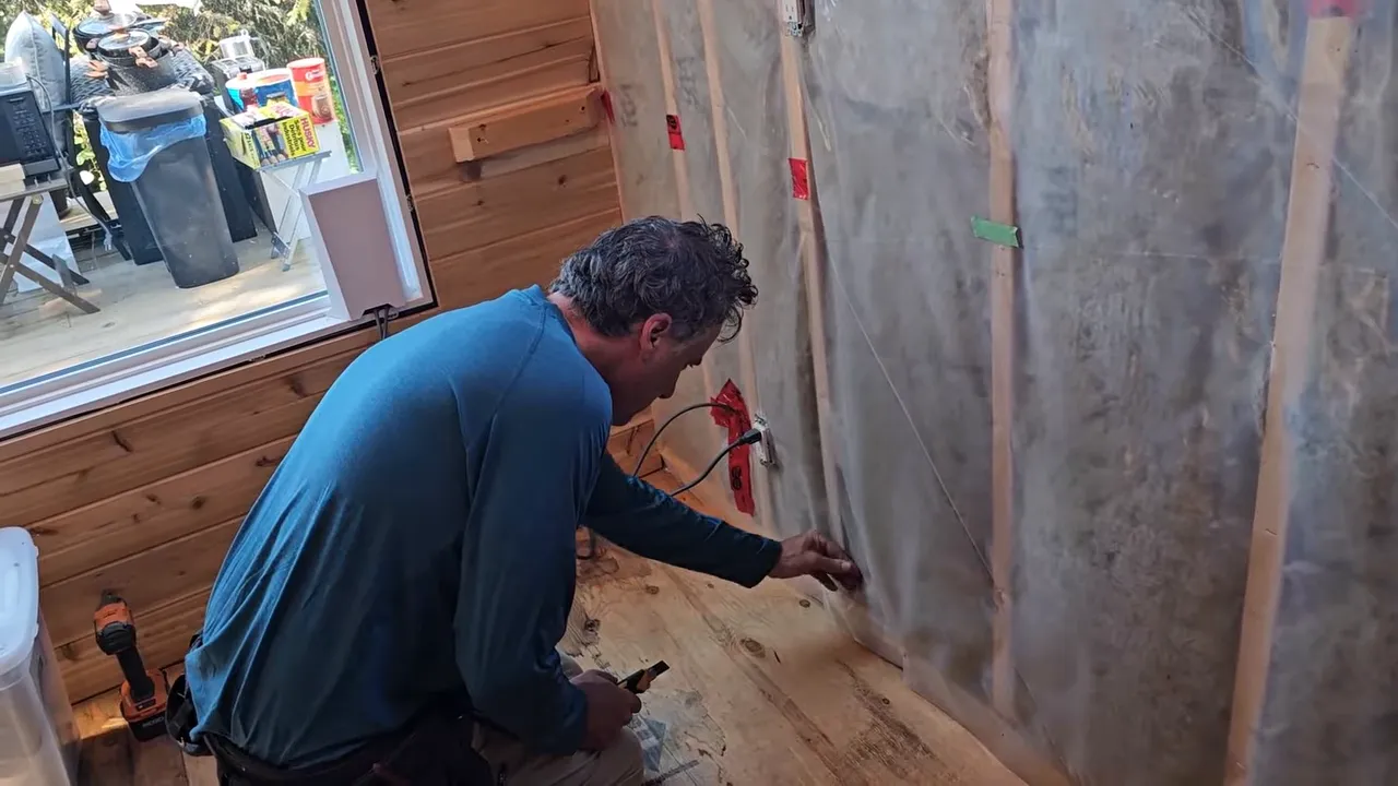 Builder applying tape to seal vapor barrier holes on a framed interior wall