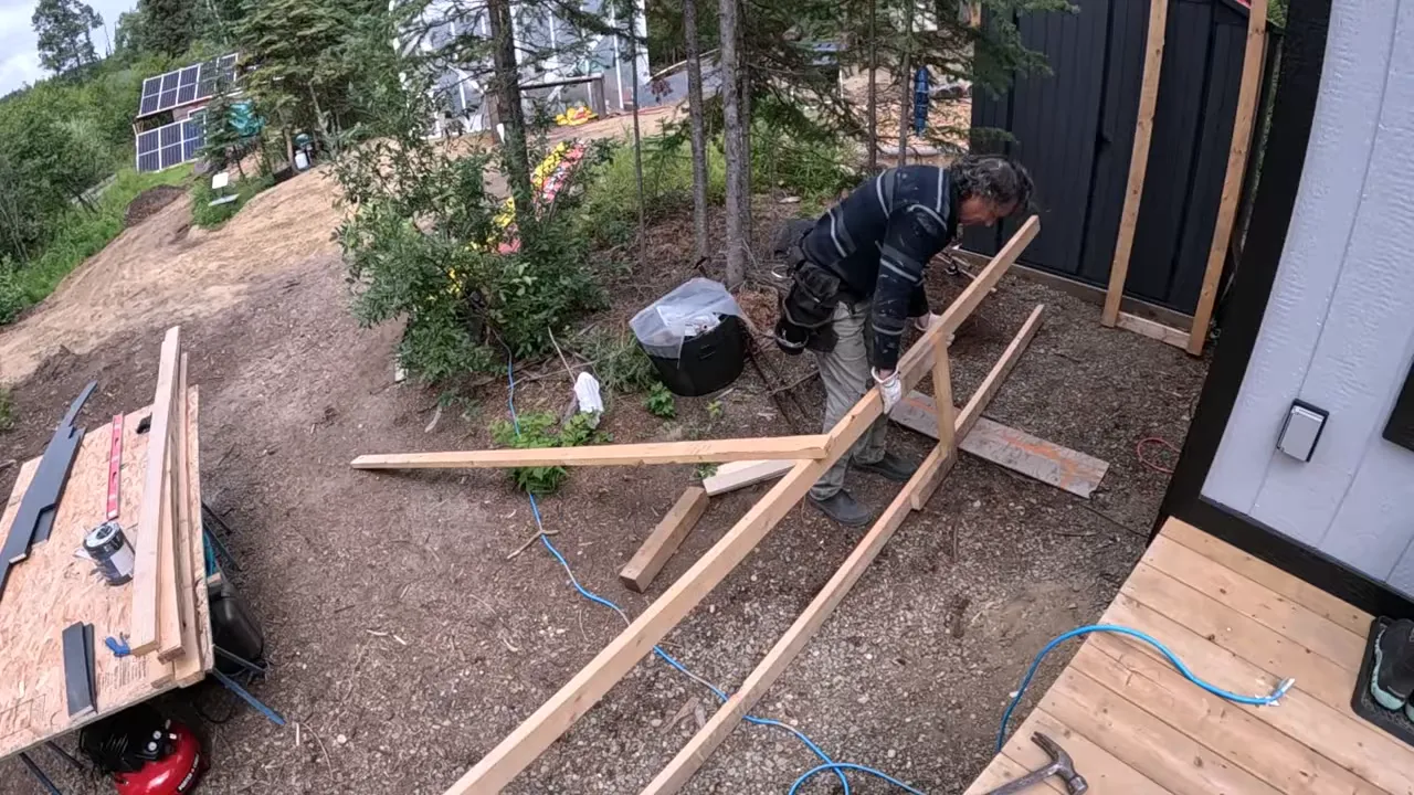 Completed custom scaffold with outriggers on sloping ground beside the cabin showing twin platforms and supports