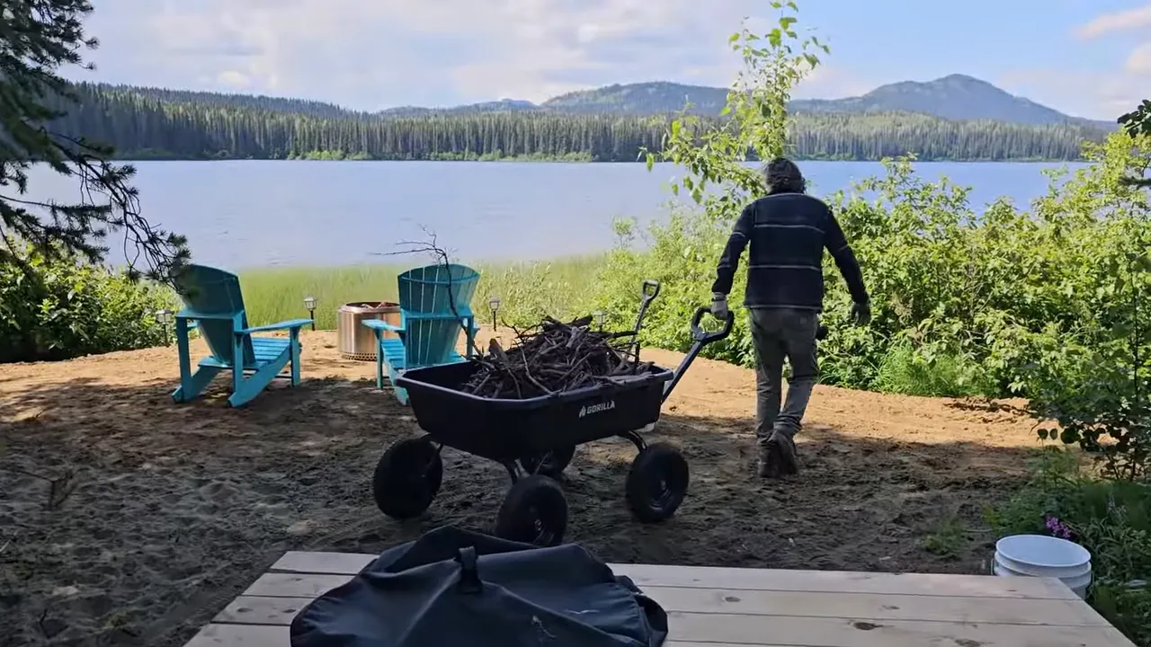 Person walking toward the lakeshore pulling a wagon of sticks with two chairs by the water