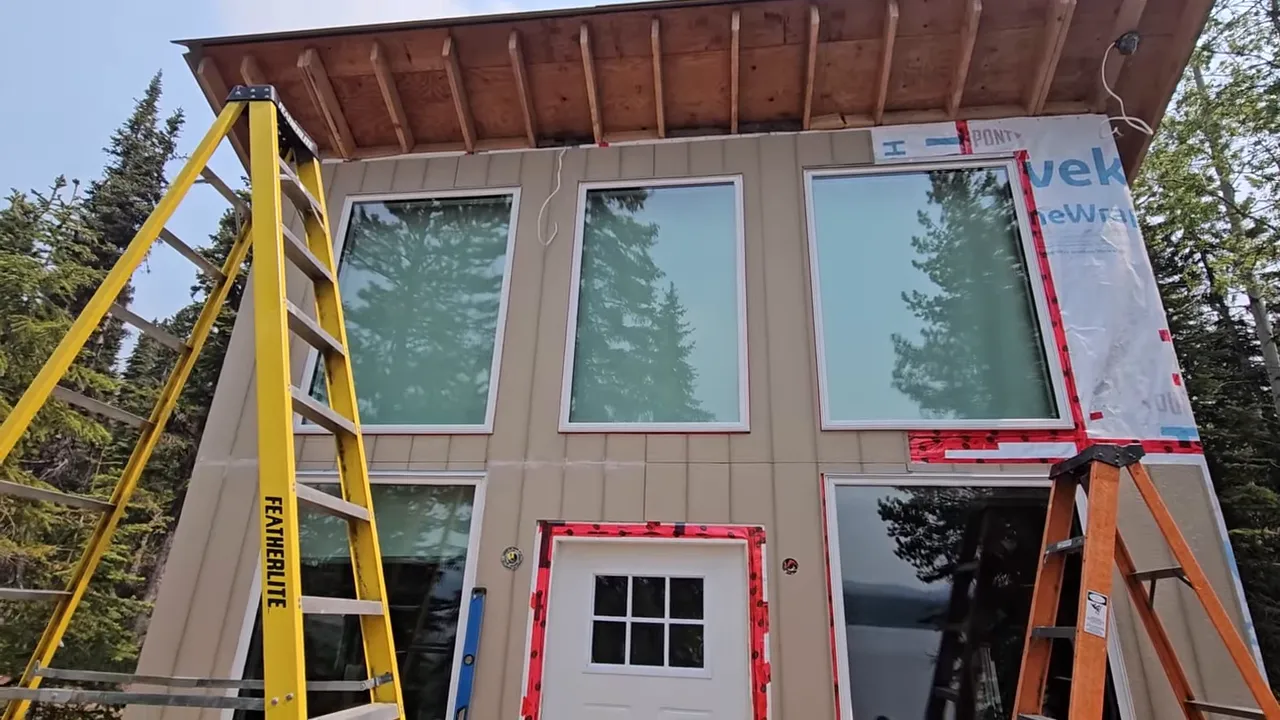 Off Grid Life Canada: Building a Tiny Cabin on Our Remote Island – Biggest Transformation Yet! - S4 Ep8 11 Close view of three large front windows and beige siding with taped seams and reflections of trees in the glass