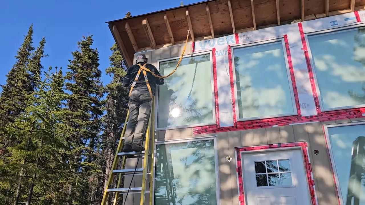 Off Grid Life Canada: Building a Tiny Cabin on Our Remote Island – Biggest Transformation Yet! - S4 Ep8 9 Worker standing on an extension ladder secured with a safety harness and tether while working on upper cabin windows