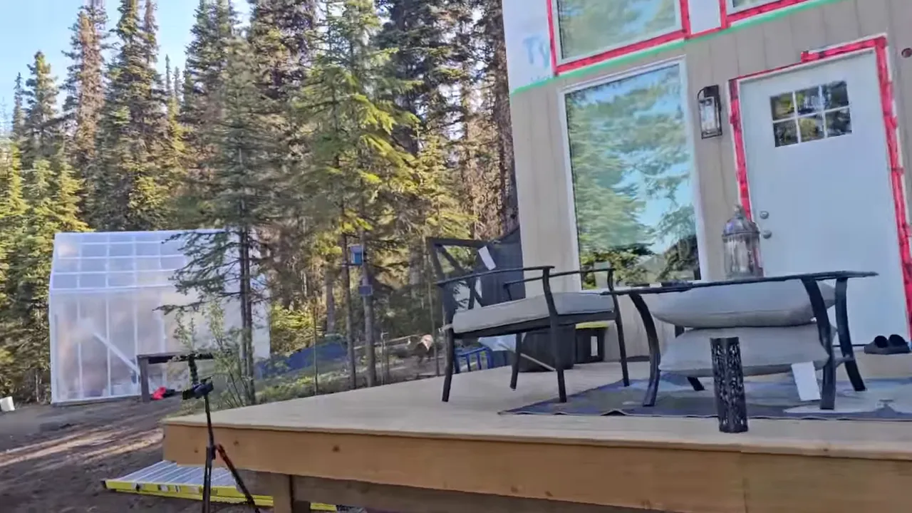 Deck with patio chairs, greenhouse and young trees at off-grid cabin homestead