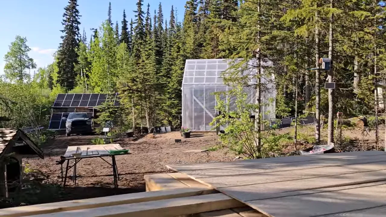 Off Grid Life Canada: Building a Tiny Cabin on Our Remote Island – Biggest Transformation Yet! - S4 Ep8 13 Wider site view showing a greenhouse, a solar panel array, a worktable and decking in a forested off‑grid setting